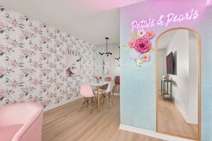 Une pièce avec un papier peint à motifs floraux, un miroir avec un cadre doré et un panneau lumineux au néon.