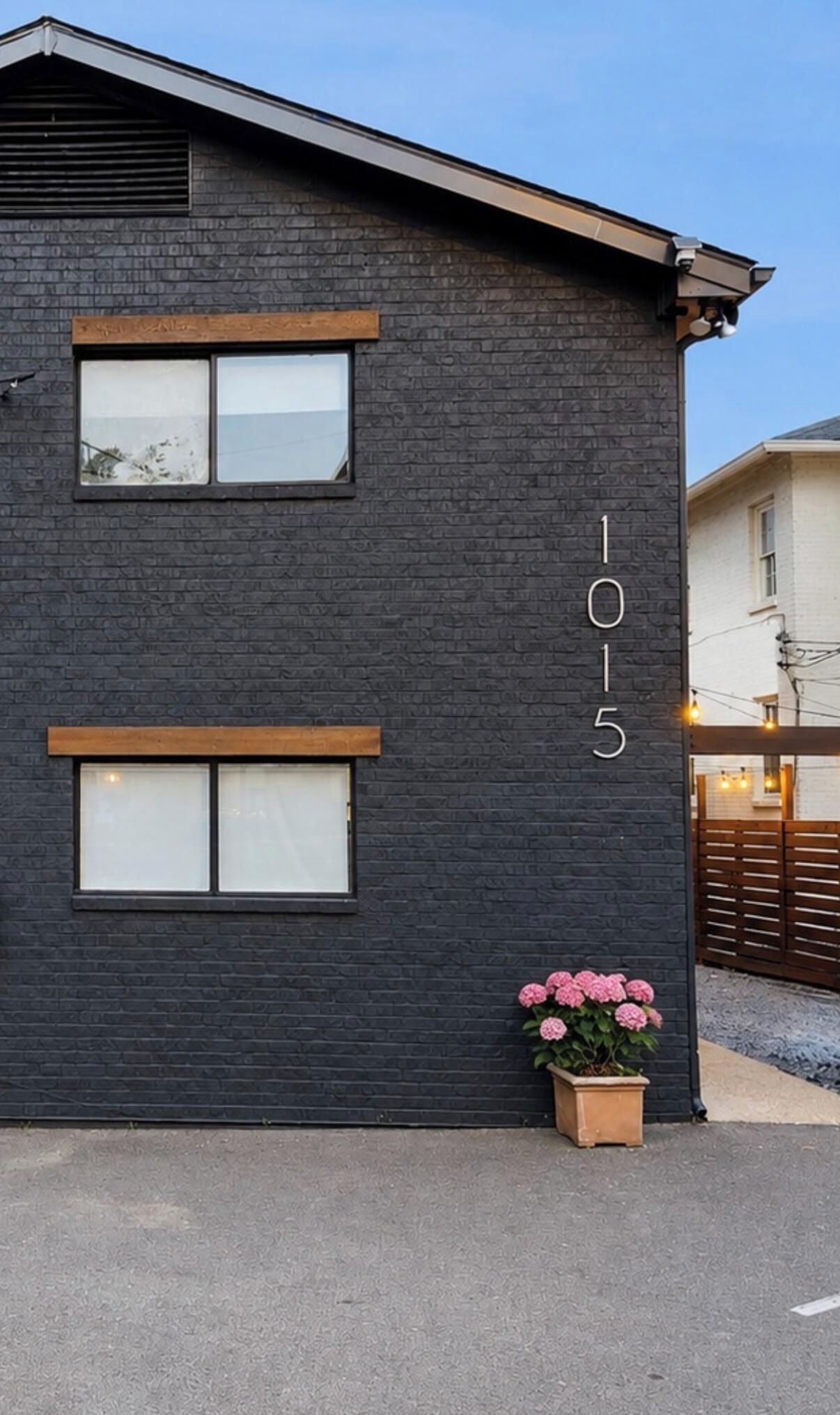 A modern building with a dark brick facade, two windows, and a flower pot with pink flowers.