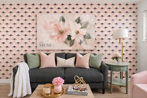 A living room with a dark sofa, decorative pillows, a coffee table with a vase, a lamp, and a bookshelf. - The Muse Girls Glam Suite Near Broadway IG Worthy (Nashville)