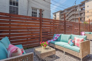 Ein Terrassenbereich mit Holzlattenzaun, Korbmöbeln und einem kleinen Tisch mit Blumenarrangement.
