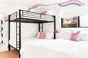 Ein Etagenbett mit weißer Bettwäsche und rosafarbenen Kissen, eine weiße Wand und ein Fenster mit Blick auf Gebäude.