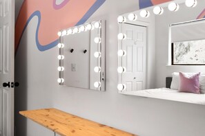 Ein Zimmer mit Schminkspiegel, Tür und einem Bett mit Kissen.
