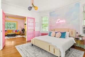 Une chambre à coucher avec un lit, une porte rose, un néon et une fenêtre avec des stores.