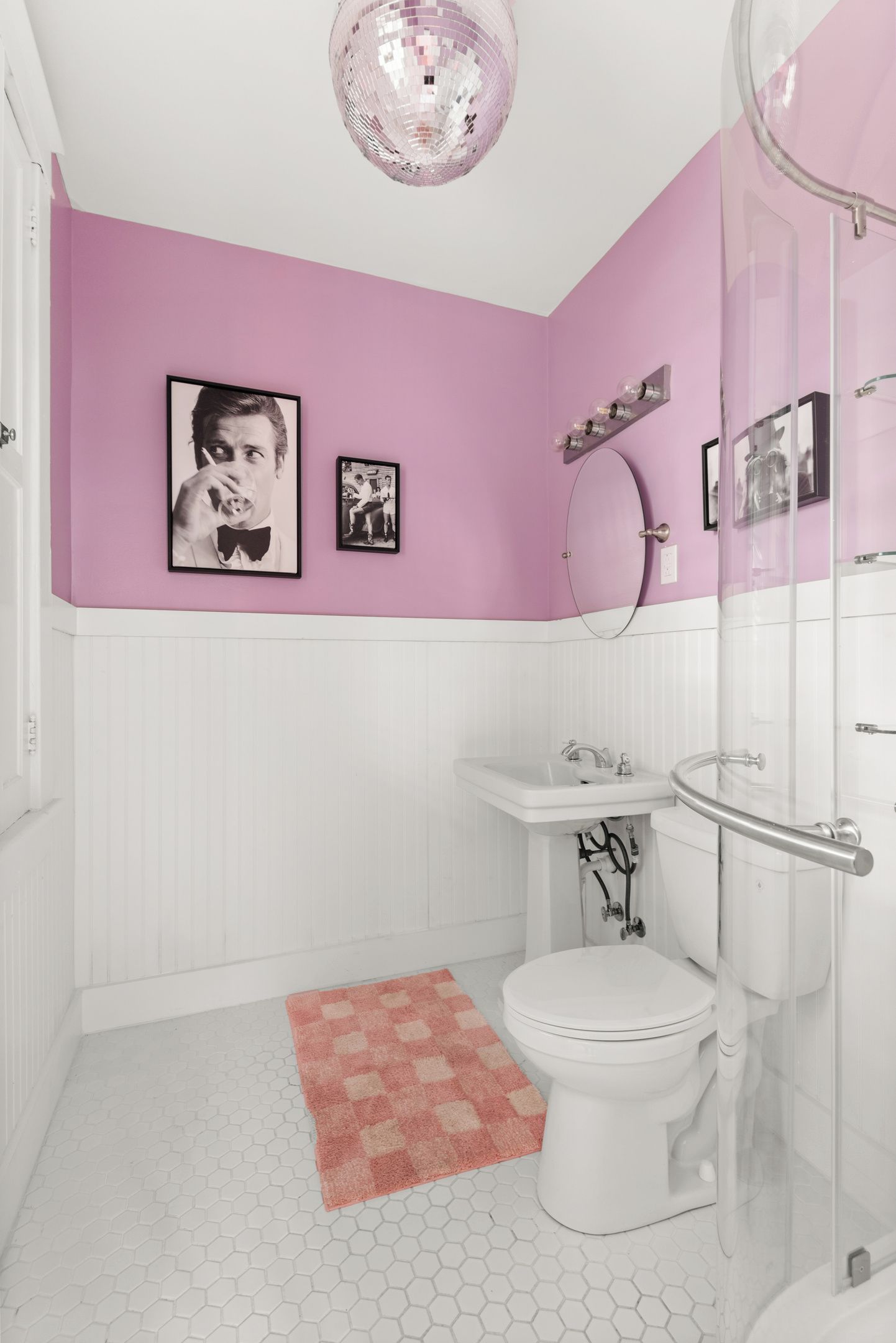 A bathroom with a white toilet, a pink wall, and a hexagonal tile floor.