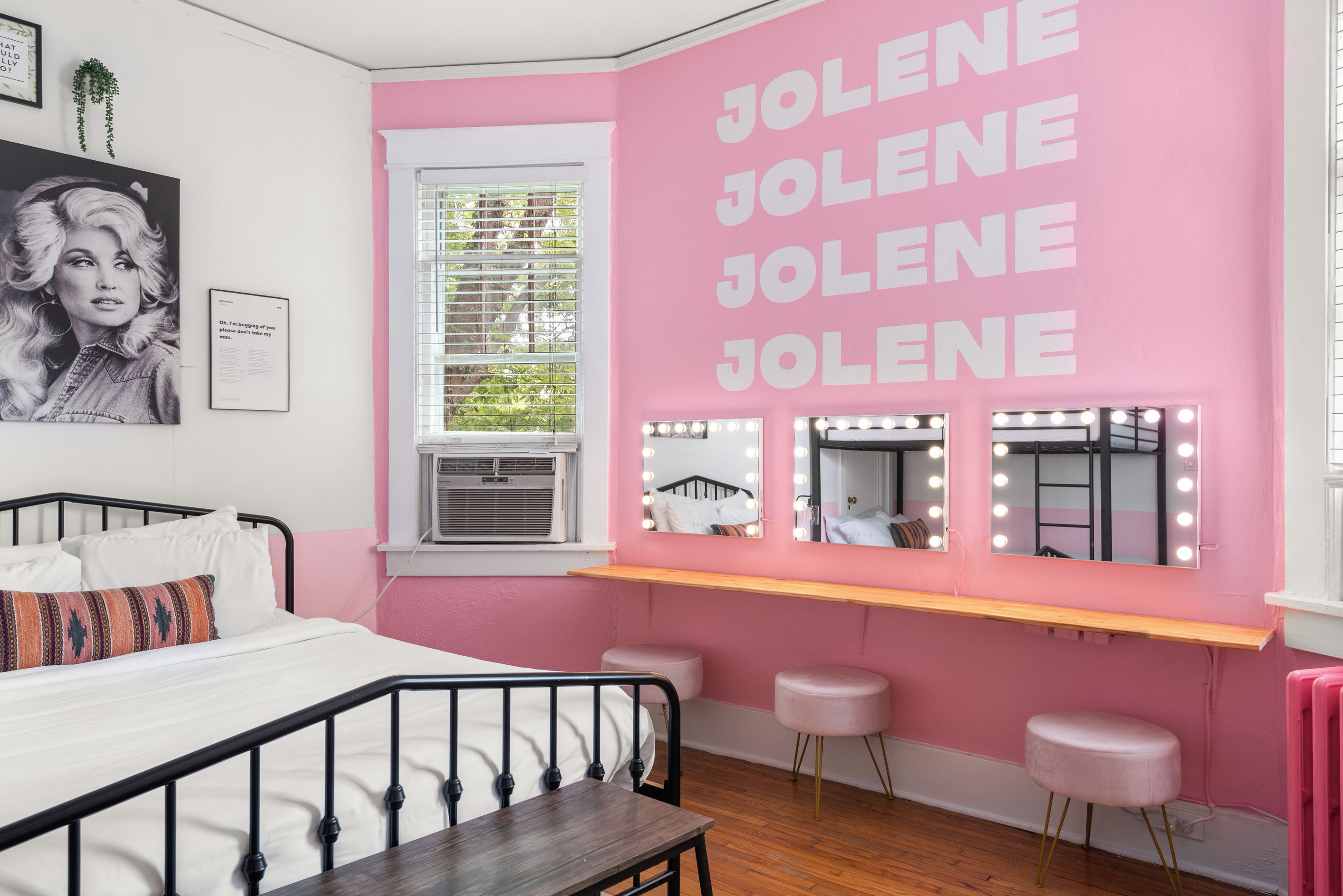 Een kamer met een bed, een kaptafel met spiegels en verlichting, en een raam met zonwering.