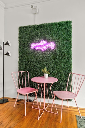 A room with a green wall, two pink chairs, a small round table, and a neon sign. - Historic Dolly + Taylor Suites, Block to Music Row (Nashville)