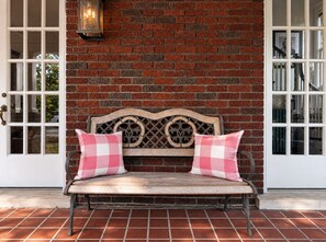 A bench with checkered cushions against a brick wall, with a lantern above and a door to the right. - Historic Dolly + Taylor Suites, Block to Music Row (Nashville)