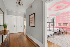 A hallway with a wooden floor, white doors, a framed sign, and a room with bunk beds and a vanity mirror. - Historic Dolly + Taylor Suites, Block to Music Row (Nashville)
