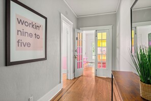 A hallway with a framed sign on the wall, wooden flooring, and a door leading to a room with colorful windows. - Historic Dolly + Taylor Suites, Block to Music Row (Nashville)