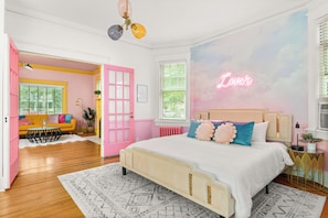 Een slaapkamer met een bed, een roze deur, een neonbord en een raam met jaloezieën.