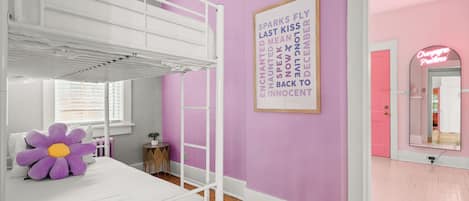 Una habitación con literas, una pared morada, un letrero de neón y un espejo.