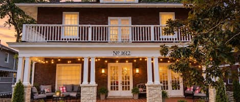 A two-story house with a balcony, numbered 1612, featuring a porch with outdoor seating and string lights.