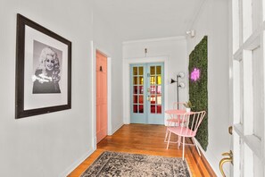 A hallway with a framed picture, a door with a letter, a plant wall, and a pink chair. - Dolly's Historic Mansion IG Worthy Near Broadway (Nashville)
