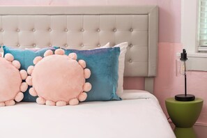 A bed with a tufted headboard, two large round pillows with pom-poms, and a bedside table with a lamp. - Taylor's Music Row Glam Near Broadway IG Worthy (Nashville)