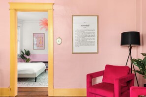 A room with a bed, a red chair, a framed text on the wall, and a door leading to another room. - Dolly + Taylor Glam Girls Trip Music Row IG Worthy (Nashville)
