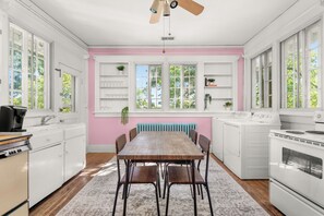 A kitchen with a wooden table, chairs, white cabinets, a pink wall, and a window with a view of trees. - Dolly + Taylor Glam Girls Trip Music Row IG Worthy (Nashville)