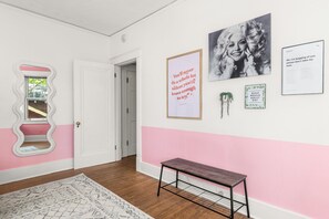 A hallway with a white door, a pink wall, and a bench. There are framed pictures and a mirror on the wall. - Dolly + Taylor Glam Girls Trip Music Row IG Worthy (Nashville)