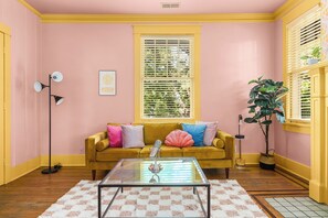 A room with a yellow sofa, a glass coffee table, a pink wall, and a window with blinds. - Dolly + Taylor Glam Girls Trip Music Row IG Worthy (Nashville)