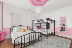 Ein Schlafzimmer mit Etagenbetten, einem rosafarbenen Heizkörper und einem Spiegel mit geschwungener Rahmung.