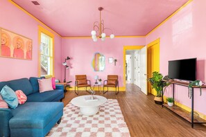 Ein Wohnzimmer mit einem blauen Sofa, einem Couchtisch und einem Fernseher auf einem Holzboden.