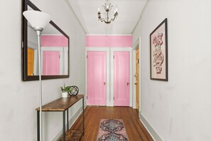A hallway with a wooden floor, a bench, a mirror, a chandelier, and pink doors. - Historic Mansion Dolly Glam Near Broadway IGWorthy (Nashville)