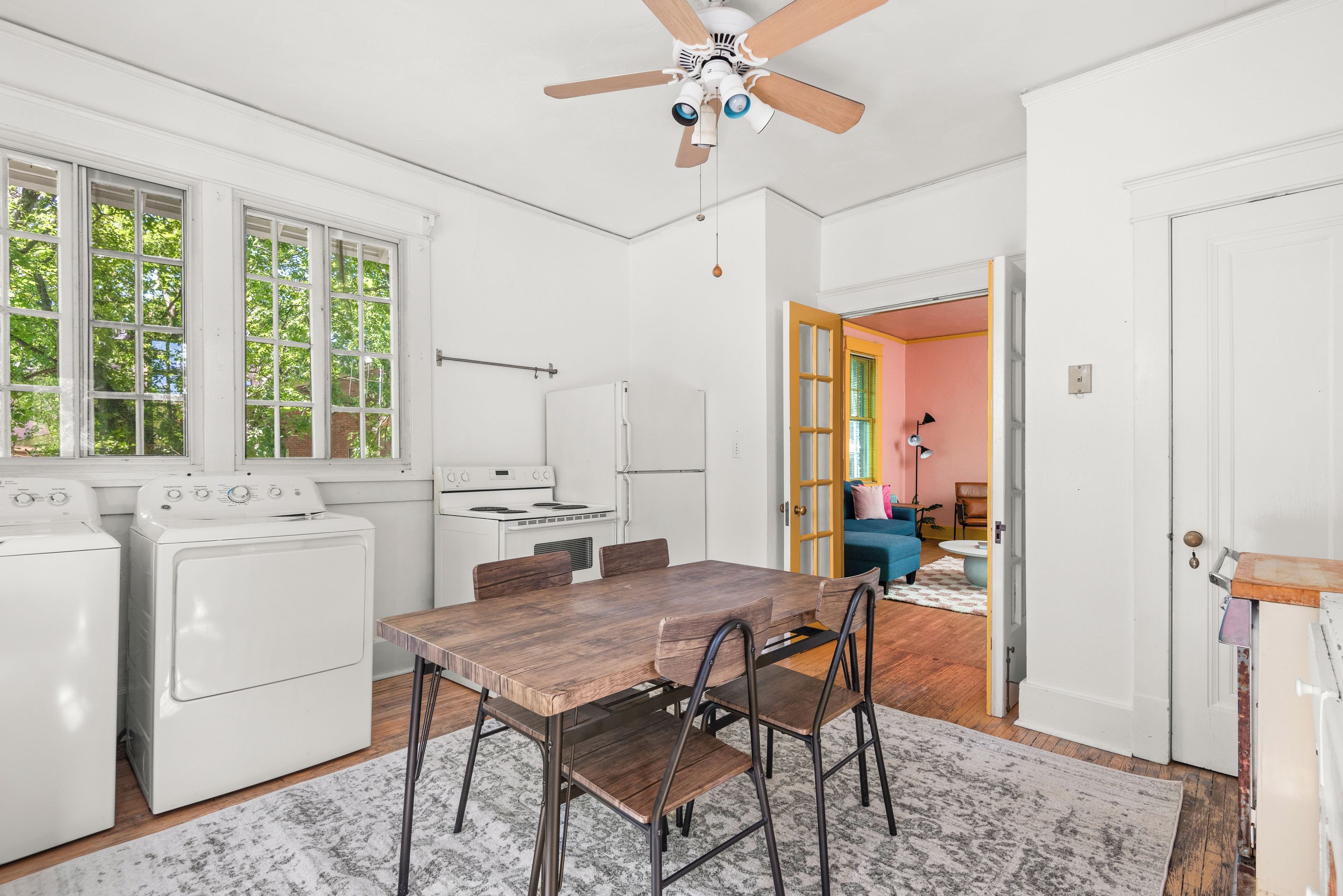 A compact kitchen with white appliances, a wooden dining table, and a ceiling fan.