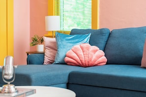 A blue sofa with pink and blue cushions, a white lamp, and a small plant on a side table. - Historic Mansion Dolly Glam Near Broadway IGWorthy (Nashville)