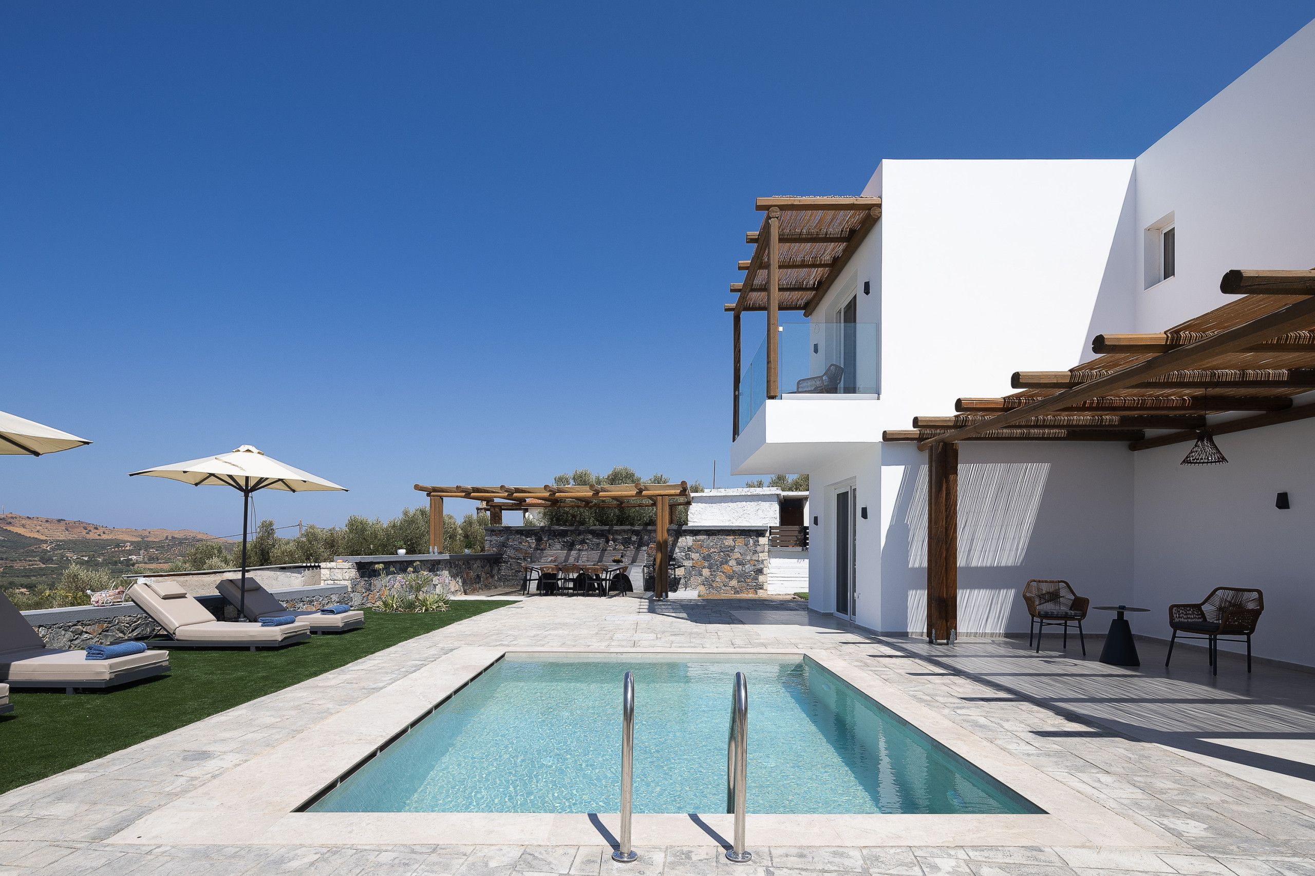 Een modern buitenzwembad met een pergola, ligbedden en een stenen muur.