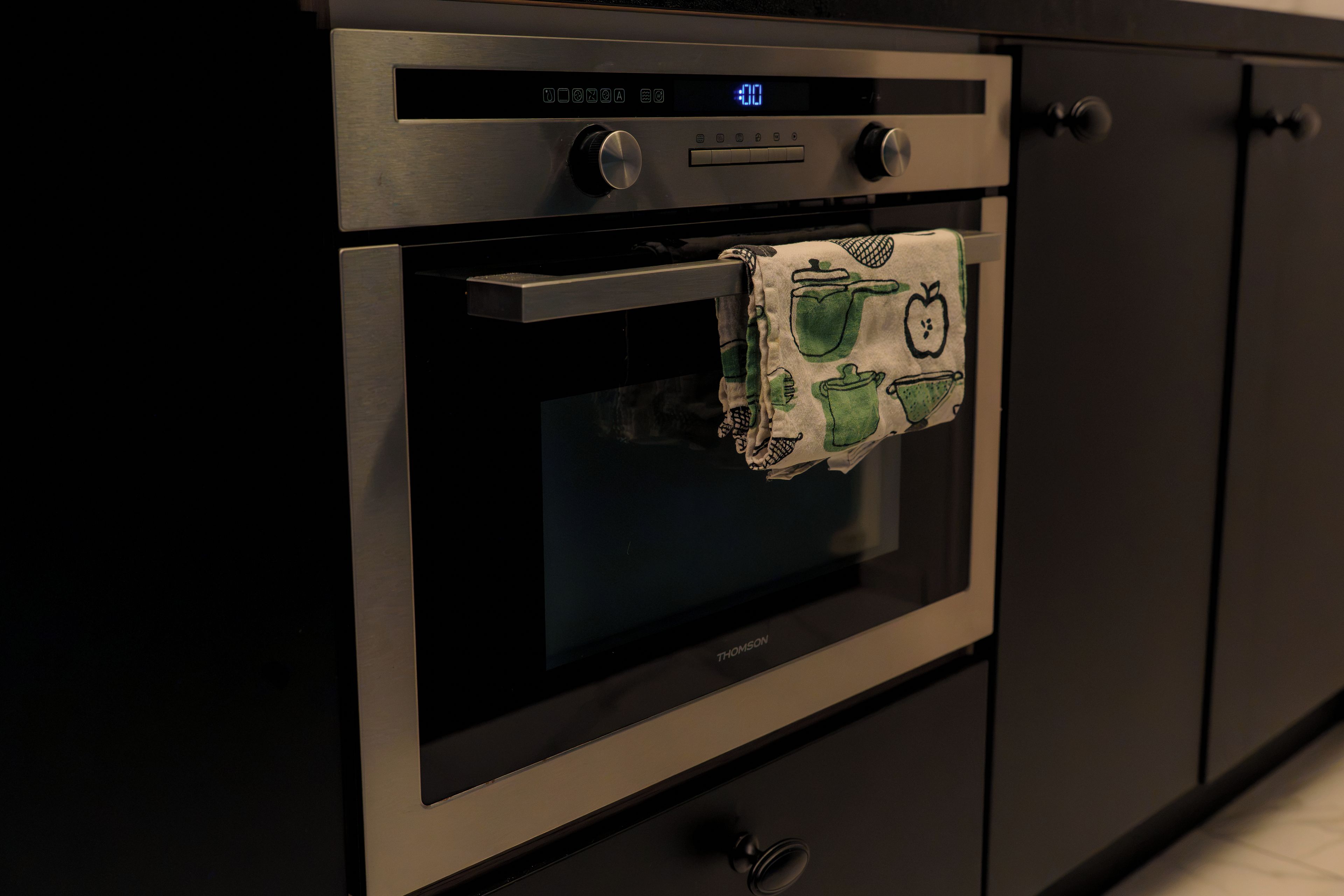 Une cuisine équipée d’un four en acier inoxydable, d’une horloge numérique et d’une serviette accrochée à la porte du four.