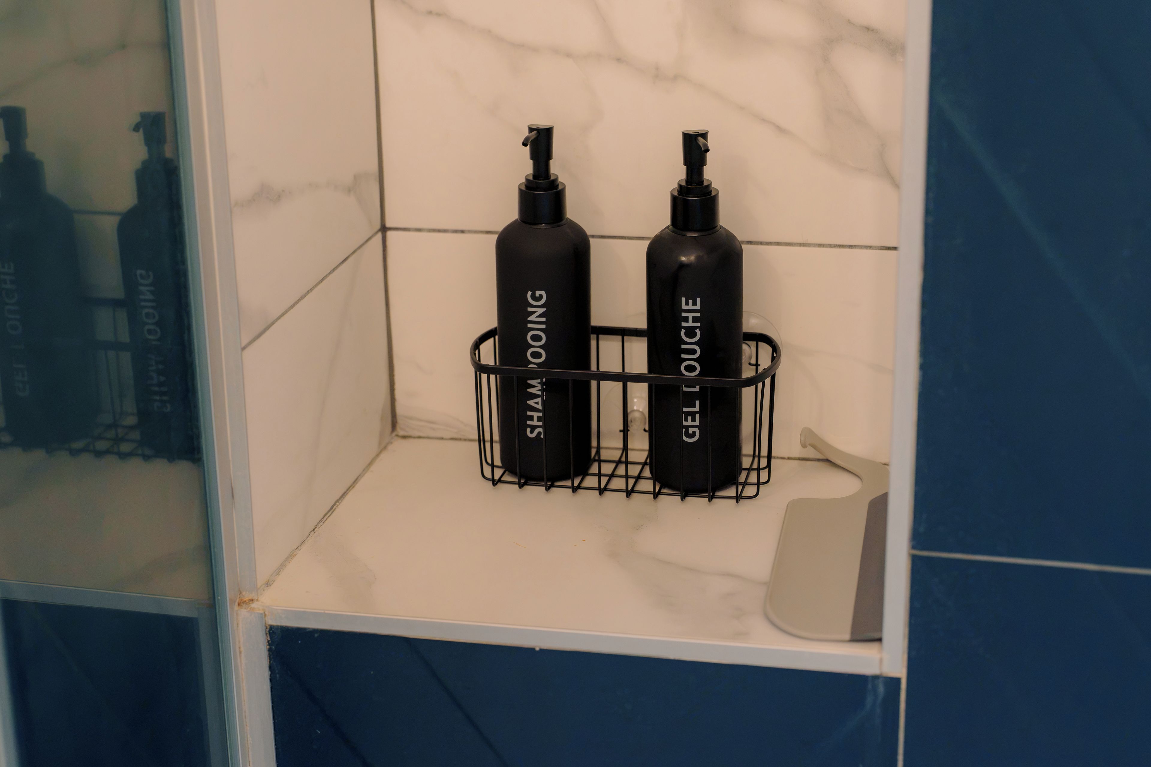 Une étagère de salle de bain avec deux bouteilles noires étiquetées « SHAMPOO » et « GEL LOUCHE ».