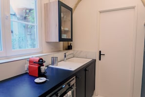 Eine kleine Küche mit integriertem Espressomaschine, Spüle und Fenster.