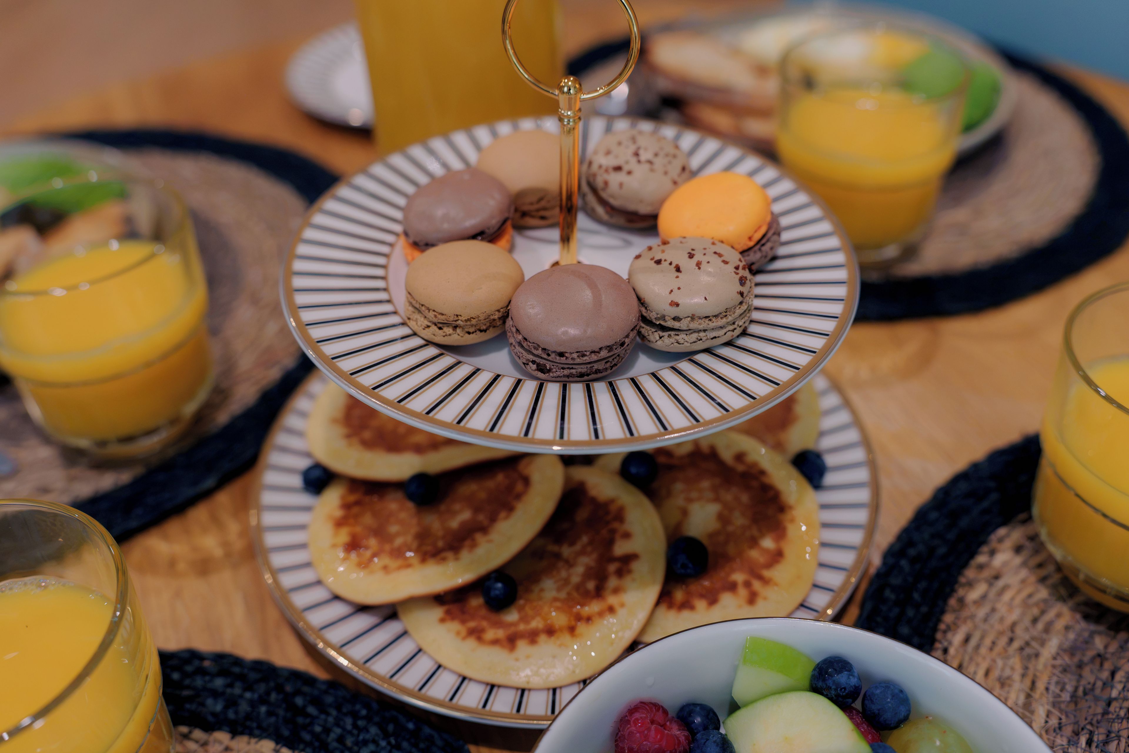 A breakfast setting with a plate of macarons, pancakes, and a bowl of fruit.