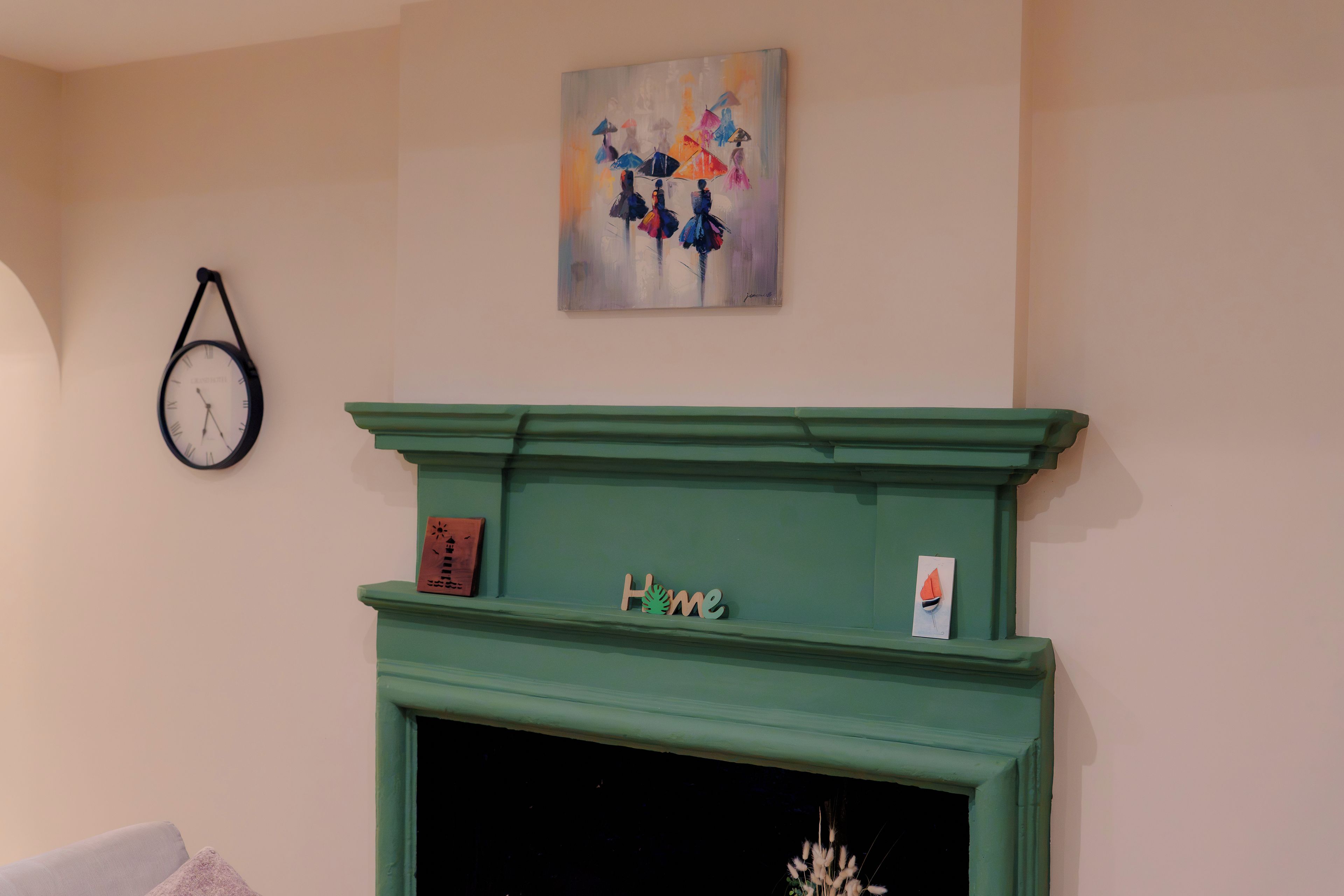 A room with a green fireplace, a clock on the wall, and a painting above it.