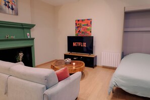 Ein Wohnzimmer mit Kamin, einem Fernseher, der 'NETFLIX' anzeigt, einem Sofa, einem Couchtisch und einem Bett.