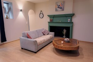 Ein Wohnzimmer mit einem grauen Sofa, einem runden Holztisch, einem grünen Kamin und einer Wanduhr.