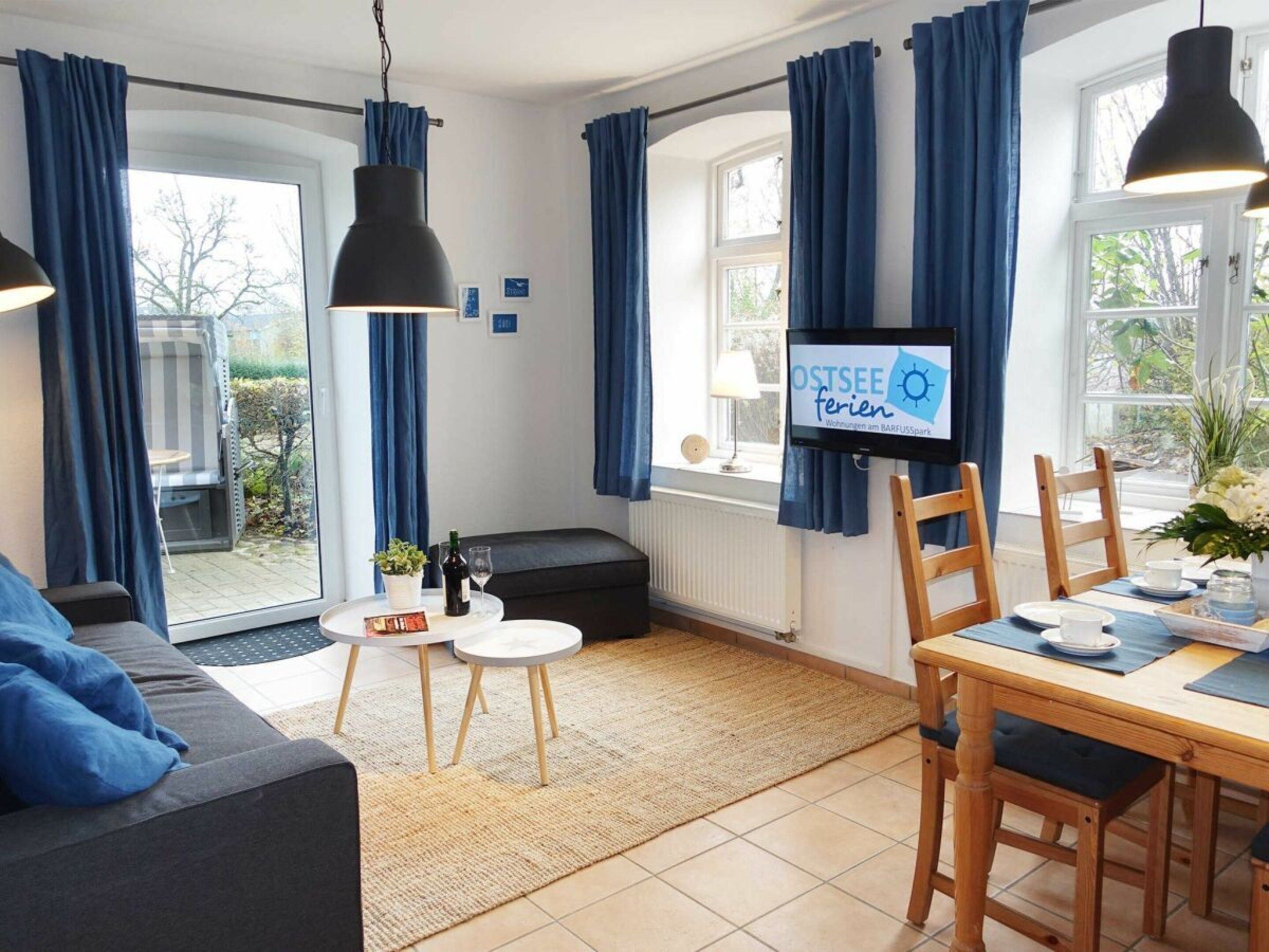 Un salon moderne avec un canapé, une table à manger et des chaises, un téléviseur et une vue sur l’extérieur.