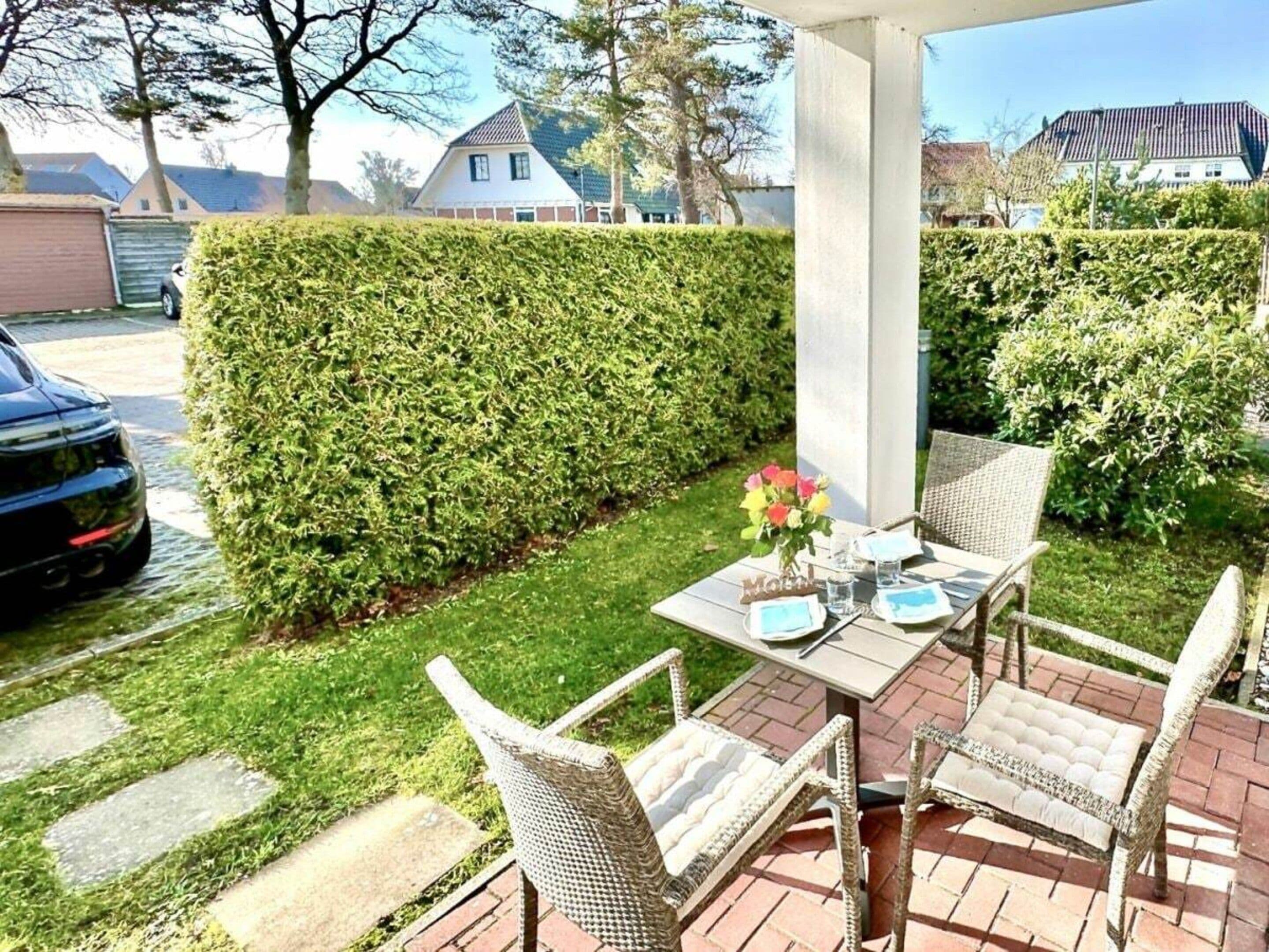 Un patio con mobiliario de mimbre, una mesa lista para comer y un seto bien cuidado.