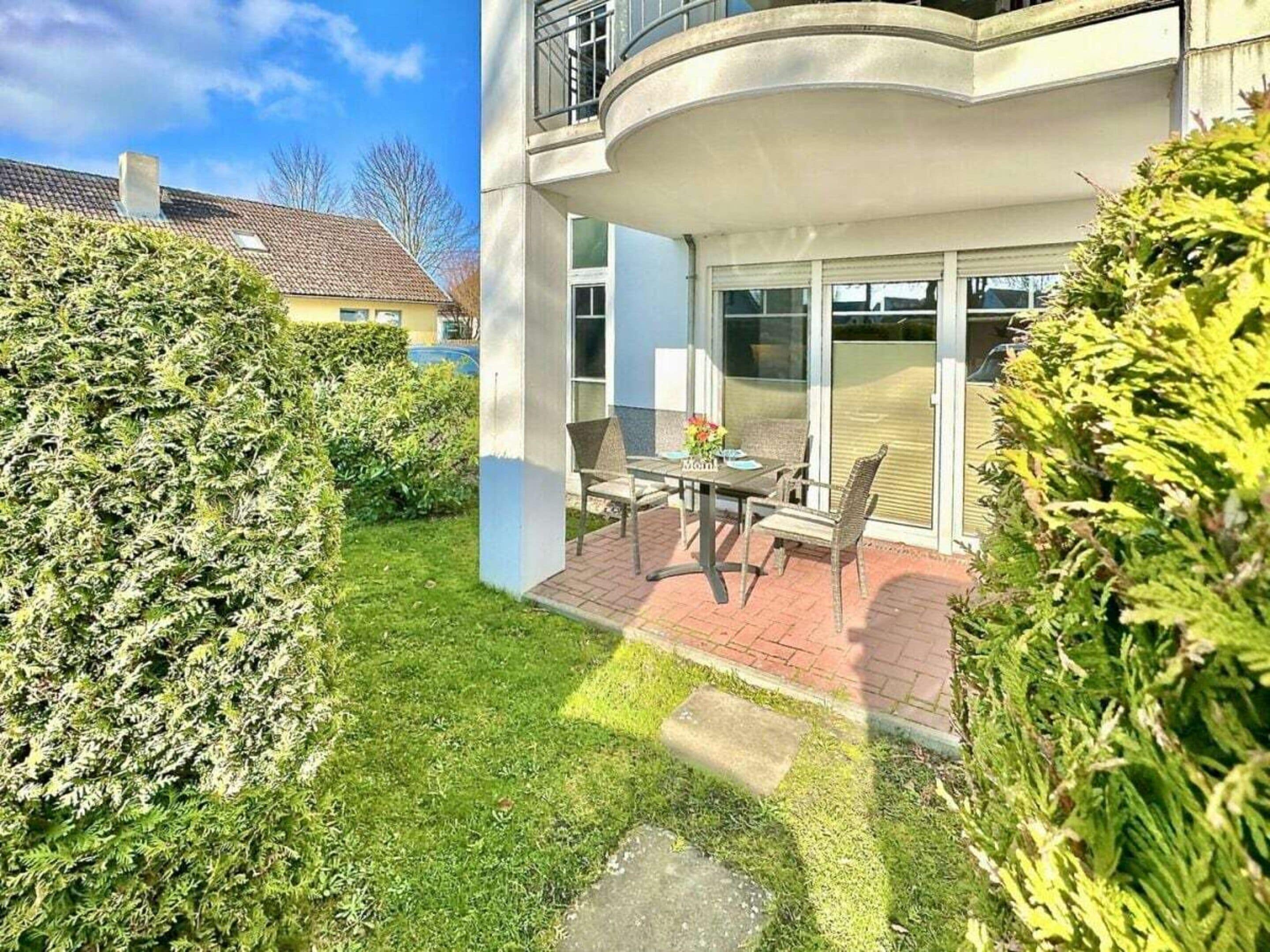 A residential building with a patio area featuring a table and chairs, surrounded by well-maintained hedges.