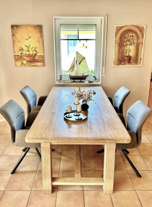 A dining table with six chairs, a window with a sailboat view, and two paintings on the walls. - Holiday Apartment With 2 Bedrooms (Zingst)