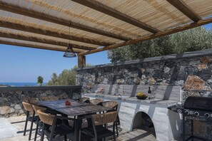 Eine Terrasse im Freien mit einer Steinwand, einer Grillstation und einem Tisch mit Stühlen.
