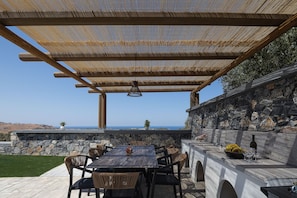An outdoor patio with a table and chairs, a pergola overhead, and a stone wall. - Melora Villa 1 - With Private Pool Jacuzzi (Mylopotamos)