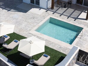 Ein rechteckiger Swimmingpool mit gefliestem Sonnendeck, umgeben von Liegestühlen und Sonnenschirmen.