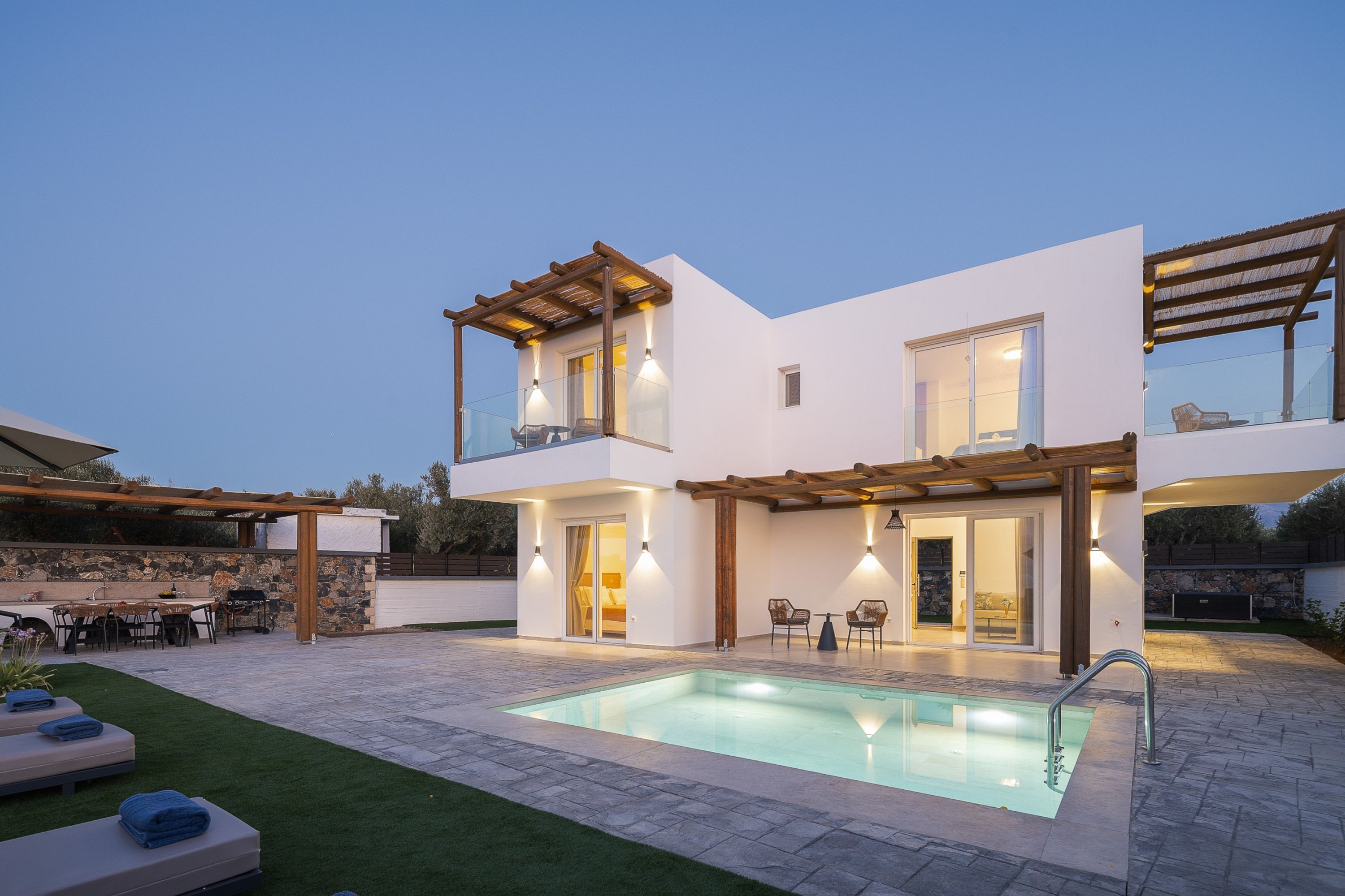 A modern two-story house with a swimming pool, outdoor seating, and a stone wall.