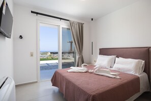 Habitació d'hotel amb llit, televisió, porta corredissa de vidre al balcó i vista al mar.