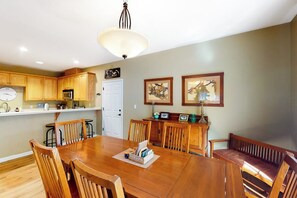 A dining area with a wooden table and chairs, a white ceiling light, wooden cabinets, and framed artwork on the wall. - Northshore Lakeview Getaway (Bass Lake)