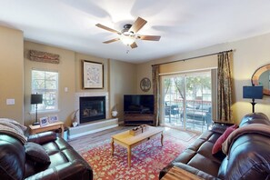 A living room with a fireplace, a television, a ceiling fan, and a large window with curtains. - Northshore Lakeview Getaway (Bass Lake)