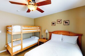 Ein Zimmer mit einem Etagenbett, einem Einzelbett, einem Nachttisch, einer Lampe und einem Deckenventilator.