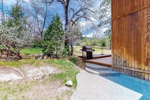 Eine Holzterrasse mit Grill, Poolbereich und Blick auf Bäume und einen klaren Himmel.
