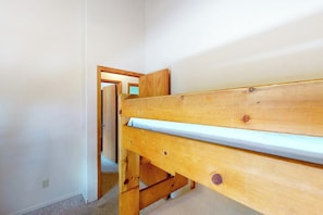 Ein Holzbett mit Etagen in einem Zimmer mit weißen Wänden und Teppichboden.