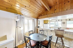 A cozy kitchen with a wooden ceiling, a round dining table with chairs, and a window with curtains. - The Lakefront Retreat (Bass Lake)